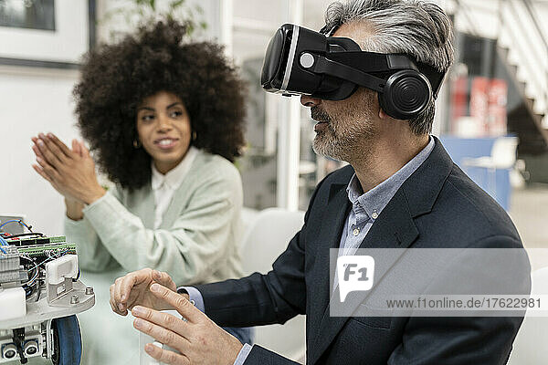 Geschäftsmann trägt Virtual-Reality-Simulator und sitzt neben einem Kollegen in der Fabrik