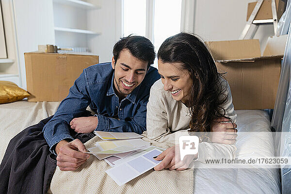 Lächelndes junges Paar wählt Farbmuster im Schlafzimmer seines neuen Zuhauses