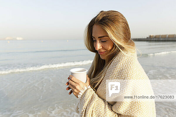 Smiling blond woman holding tea cup at beach