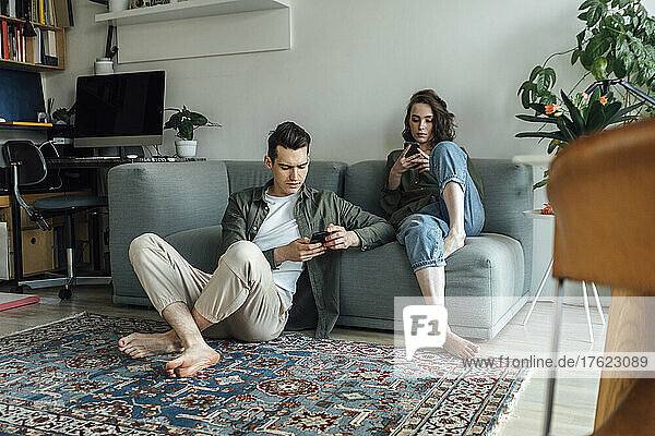 Junges Paar nutzt Smartphones im heimischen Wohnzimmer
