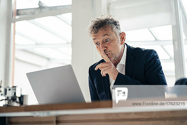 Senior businessman doing silence gesture on video call through laptop