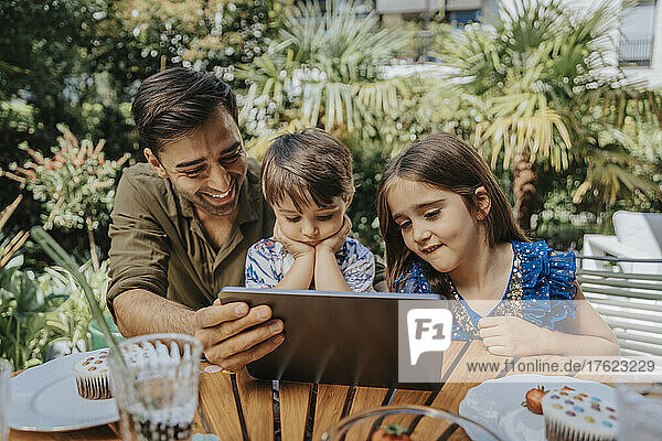 Vater und Kinder nutzen Tablet-PC im Hinterhof