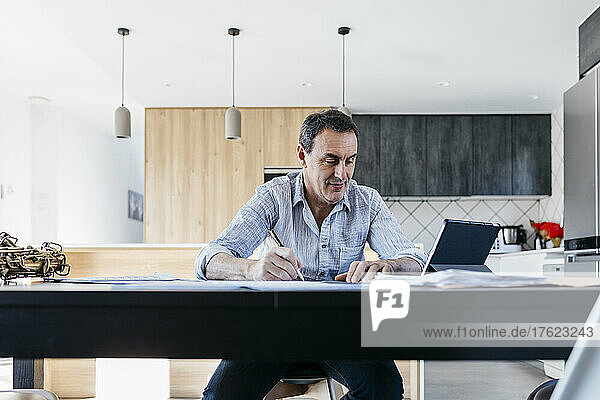 Mann schreibt und schaut auf Tablet-PC  der in der Küche sitzt