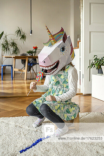 Girl in unicorn mask eating candy lollipop at home
