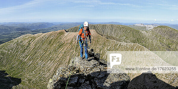 Woman wearing helmet standing on mountain on sunny day