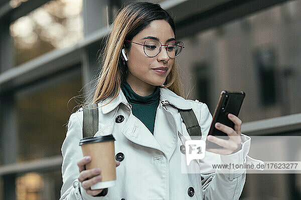 Woman holding disposable cup using mobile phone