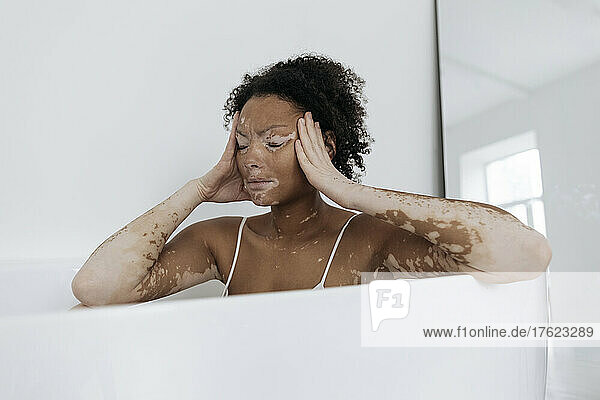 Woman having headache sitting in bathtub at home