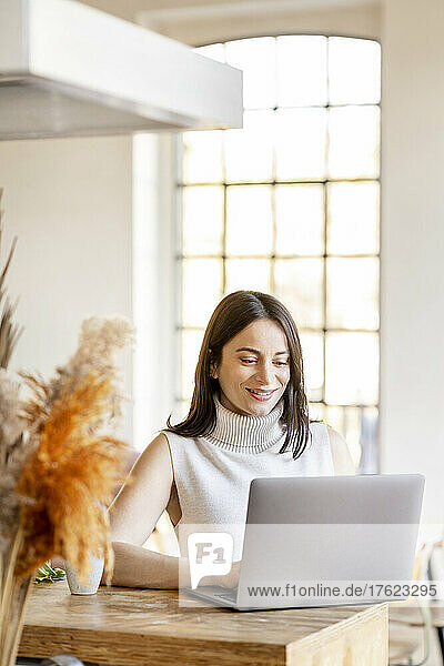 Smiling young woman working on laptop at home