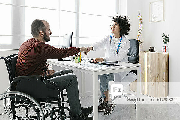 Disable patient sitting in wheelchair shaking hand with doctor at medical clinic