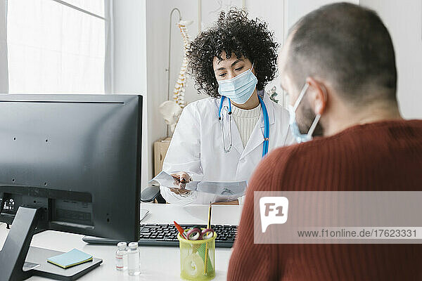 Doctor wearing protective face mask explaining X-ray report to patient at clinic
