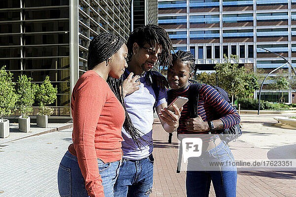 Young man showing smart phone to friends on sunny day