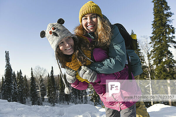 Smiling woman carrying cheerful friend enjoying in winter