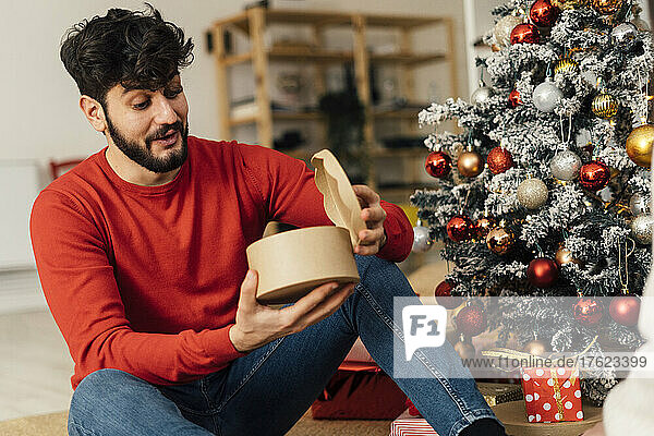 Surprised young man opening Christmas present at home