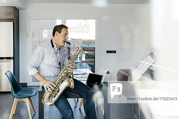 Saxophonist blowing saxophone sitting on table at home