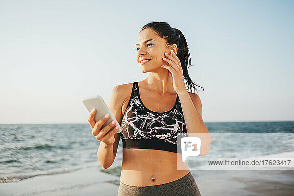 Smiling woman listening music through wireless in-ear headphones at beach