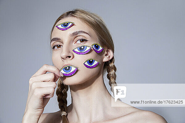 Woman with eyes stickers on face against gray background