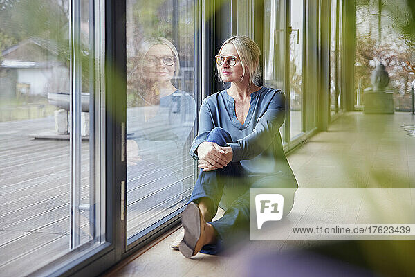 Woman sitting by glass window at home