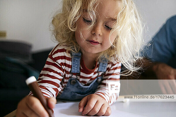 Blond boy drawing on paper by father at home