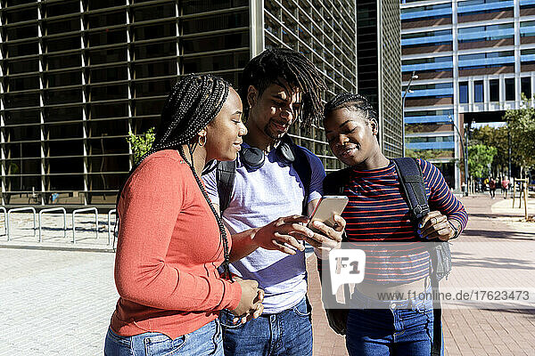 Young man sharing smart phone with friends on sunny day