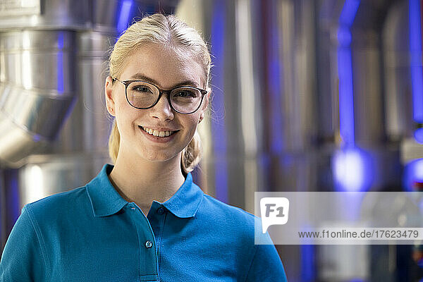 Smiling technician wearing eyeglasses standing in factory