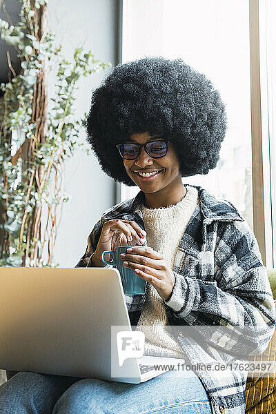 Smiling businesswoman holding mug sitting with laptop on lap
