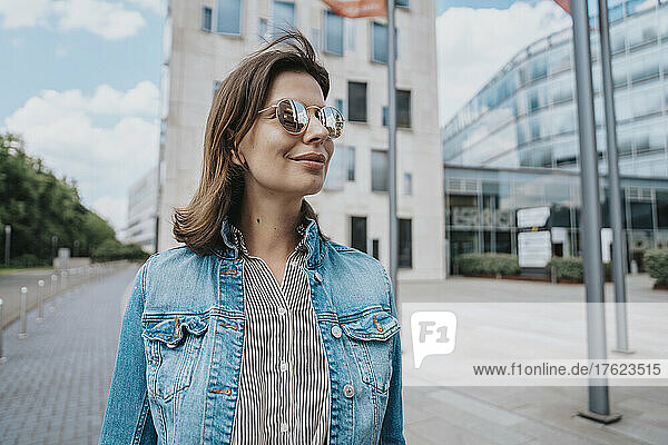 Woman in denim jacket wearing sunglasses in front of building