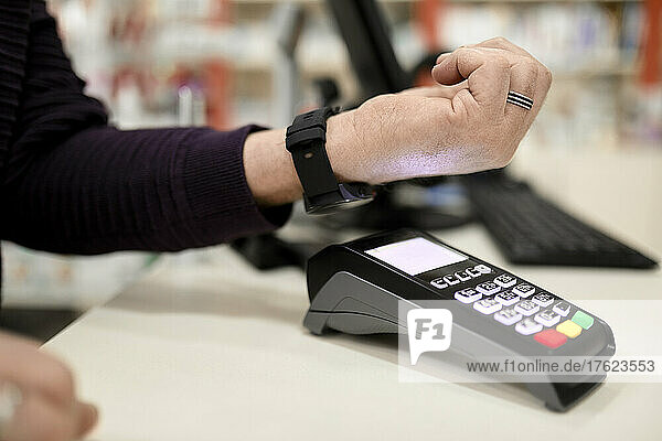 Man making contactless payment through smart watch at checkout counter in store