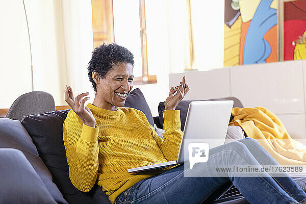 Smiling woman watching laptop with fingers crossed in living room