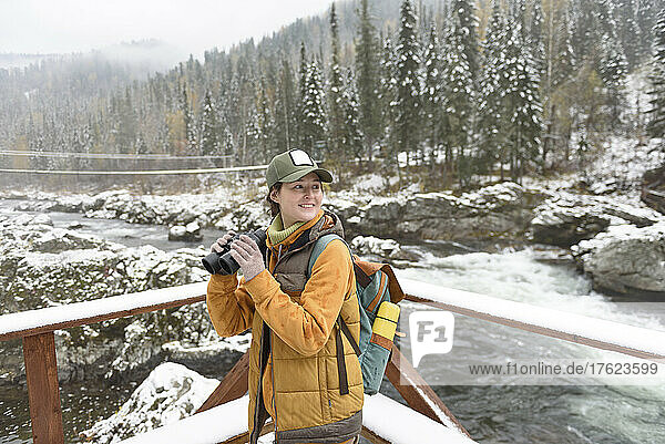 Happy woman with binocular enjoying weekend by river in winter