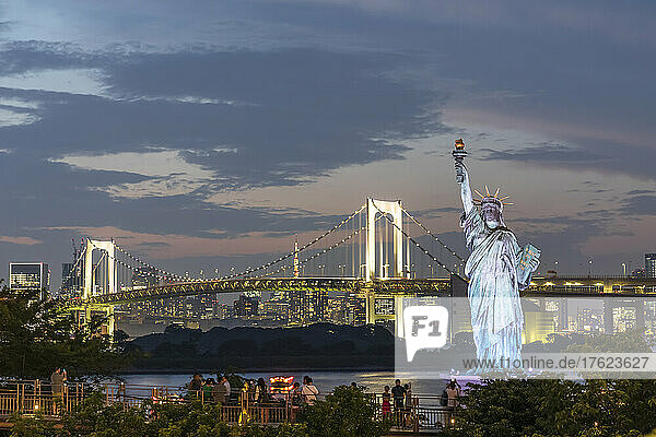 Japan  Kanto Region  Tokyo  Replica of Statue of Liberty and illuminated Rainbow Bridge at dusk