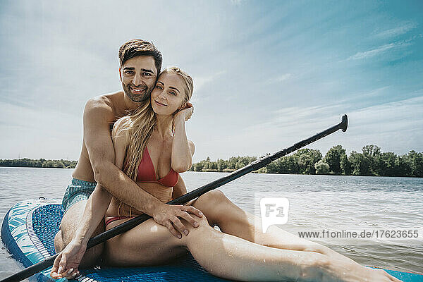 Couple sitting on paddleboard in front of sky