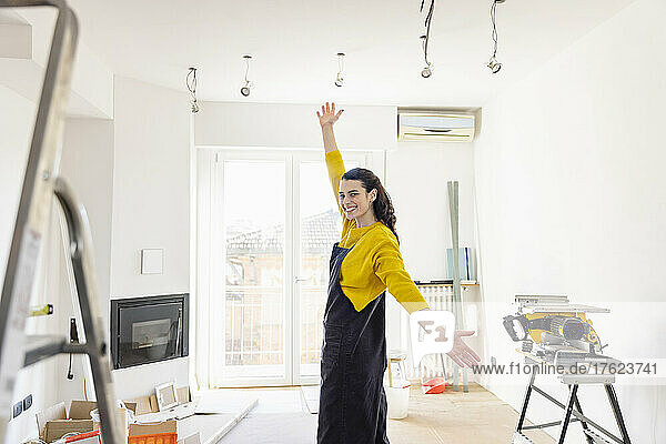 Smiling woman with arms raised standing in living room