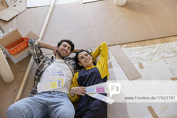 Ein glückliches Paar träumt vom Tag mit Farbmustern  die im neuen Wohnzimmer auf dem Boden liegen