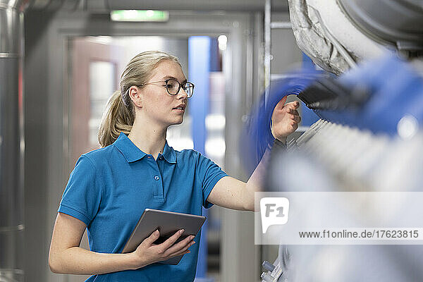Technician holding tablet PC analyzing machine in industry