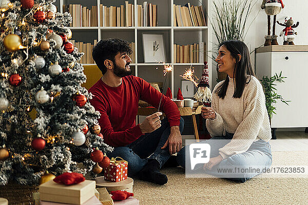 Smiling couple holding lit sparklers in living room at home