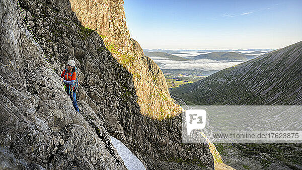 Woman climbing rocky mountain on sunny day