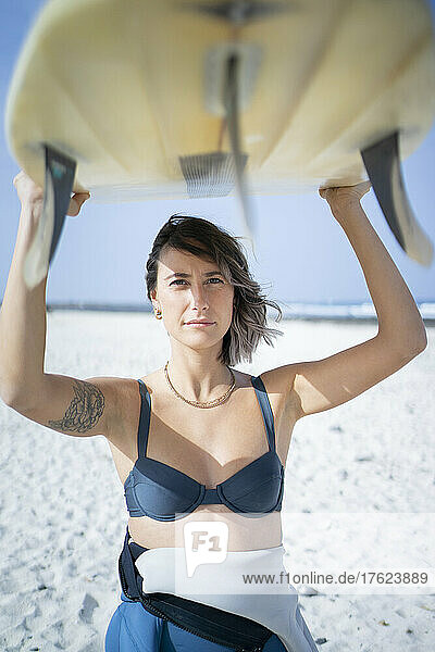 Young woman in bikini carrying surfboard at beach