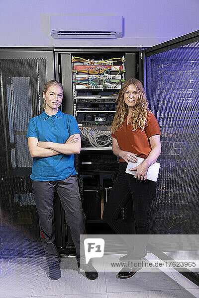 Smiling technician and trainee standing together in server room