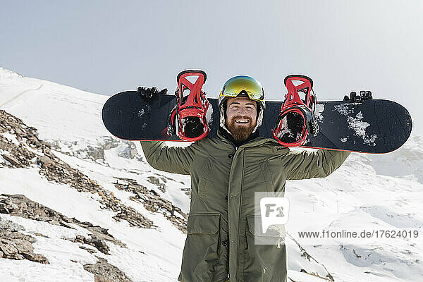 Glücklicher junger Mann  der Snowboard auf den Schultern trägt
