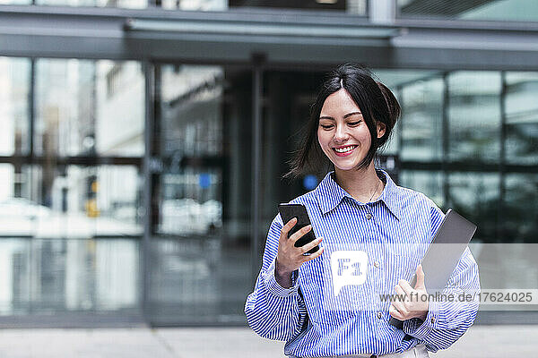 Smiling businesswoman with laptop using mobile phone
