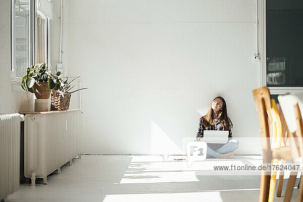 Young woman with laptop in front of wall at home