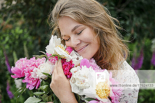 Smiling blond woman with eyes closed hugging flowers