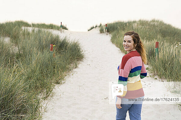Smiling beautiful young woman walking on sand