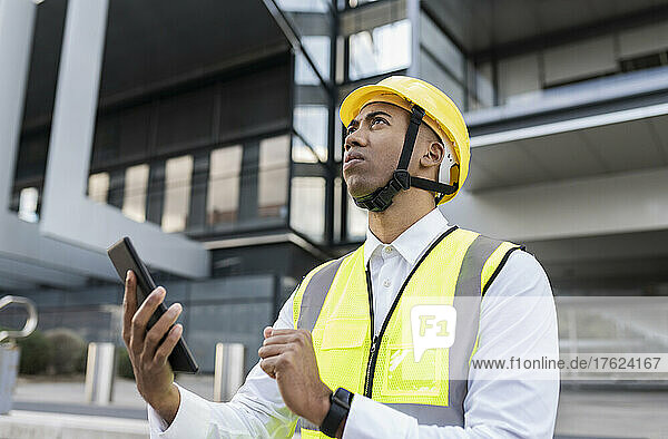 Man with hardhat holding tablet PC standing in front of building