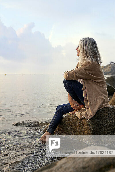 Woman sitting on rock looking at sea