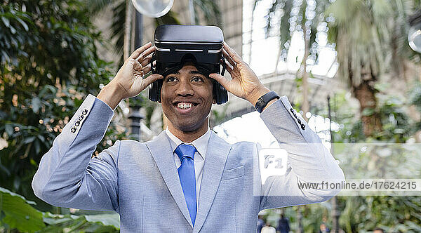 Happy businessman wearing virtual reality simulator standing by plants