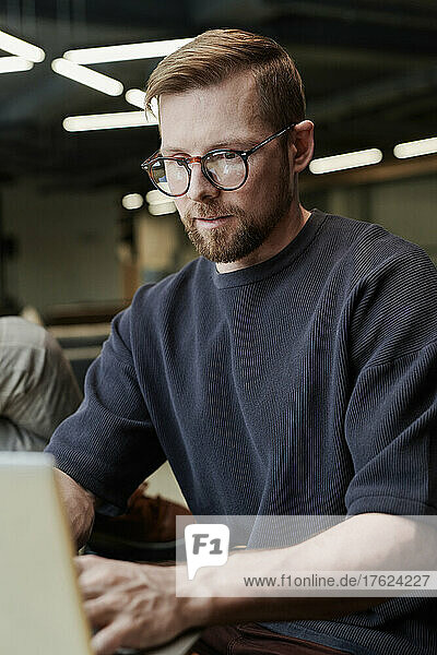 Konzentrierter Geschäftsmann mit Brille  der im Büro am Laptop arbeitet