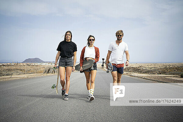 Friends with skateboards walking on road
