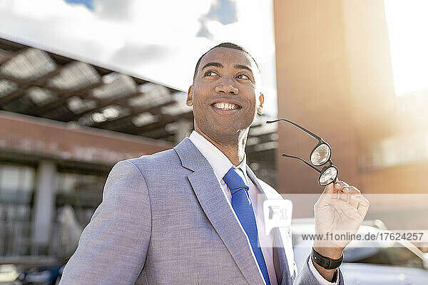 Happy businessman holding eyeglasses on sunny day