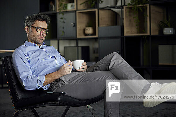 Businessman holding coffee cup sitting on chair in office